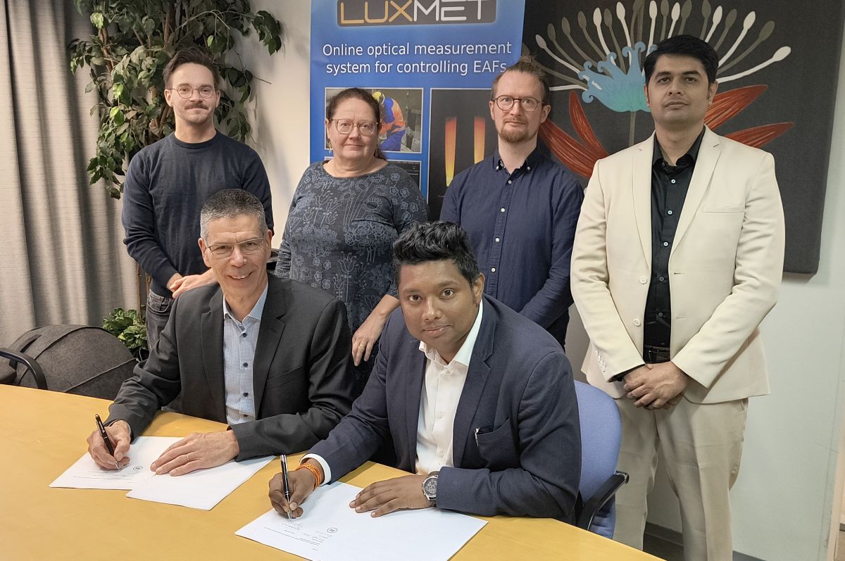 Luxmet and SRB International singing an agreement Two people signing an agreement at the table. Four people are standing behind them.