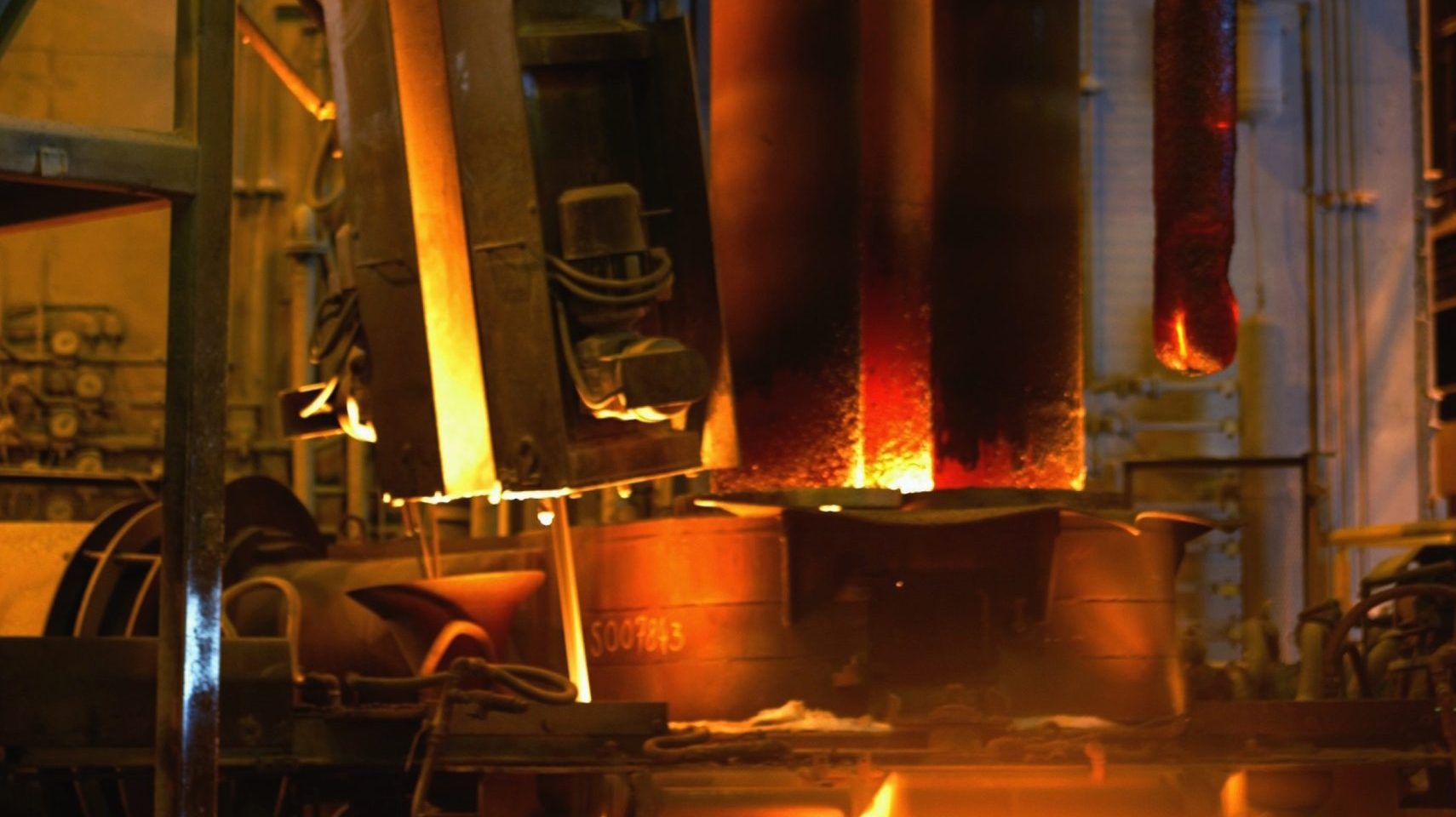 Three hot electrodes partially lowered into an electric arc furnace.