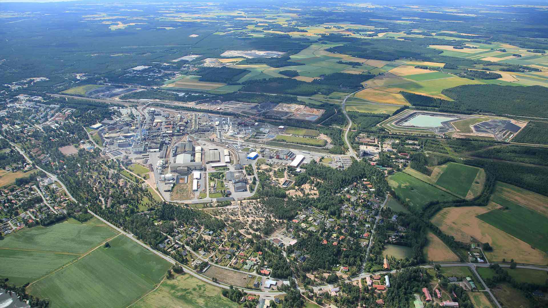 Boliden Harjavalta Aerial view of Boliden Harjavalta site with residential buildings at the front, industrial site in the center-left, and rural and forest areas at the back.